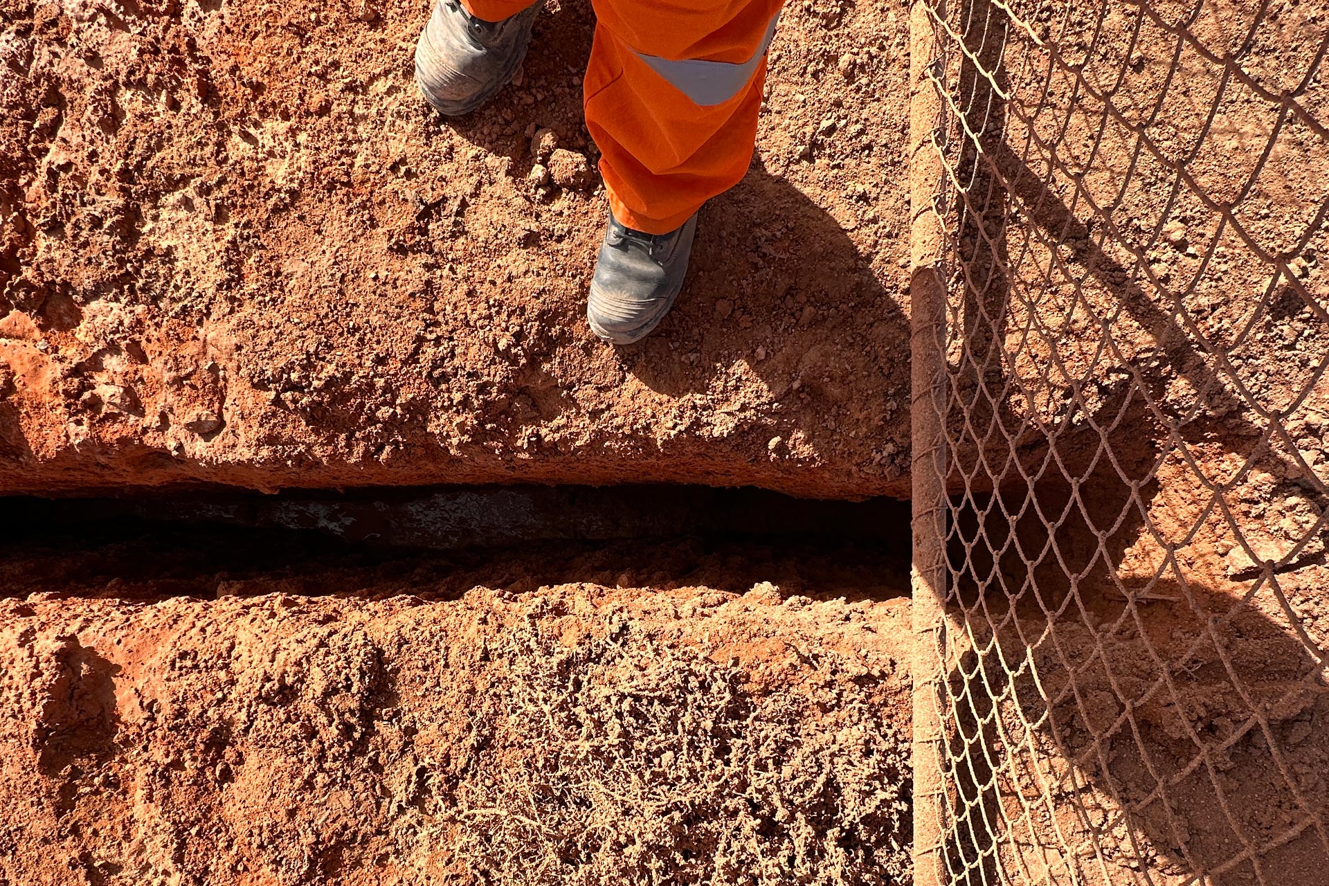 Worker inspecting slot trench abutting a gate.